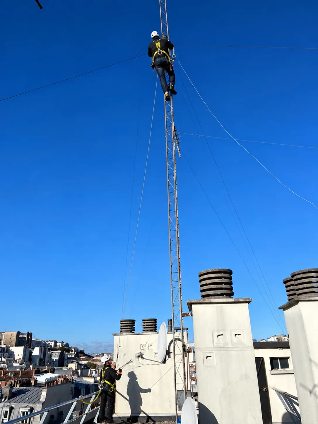 Antenniste TELEANTEN en haut d'un mât d'antenne collective, un collègue l'assurant depuis le toit