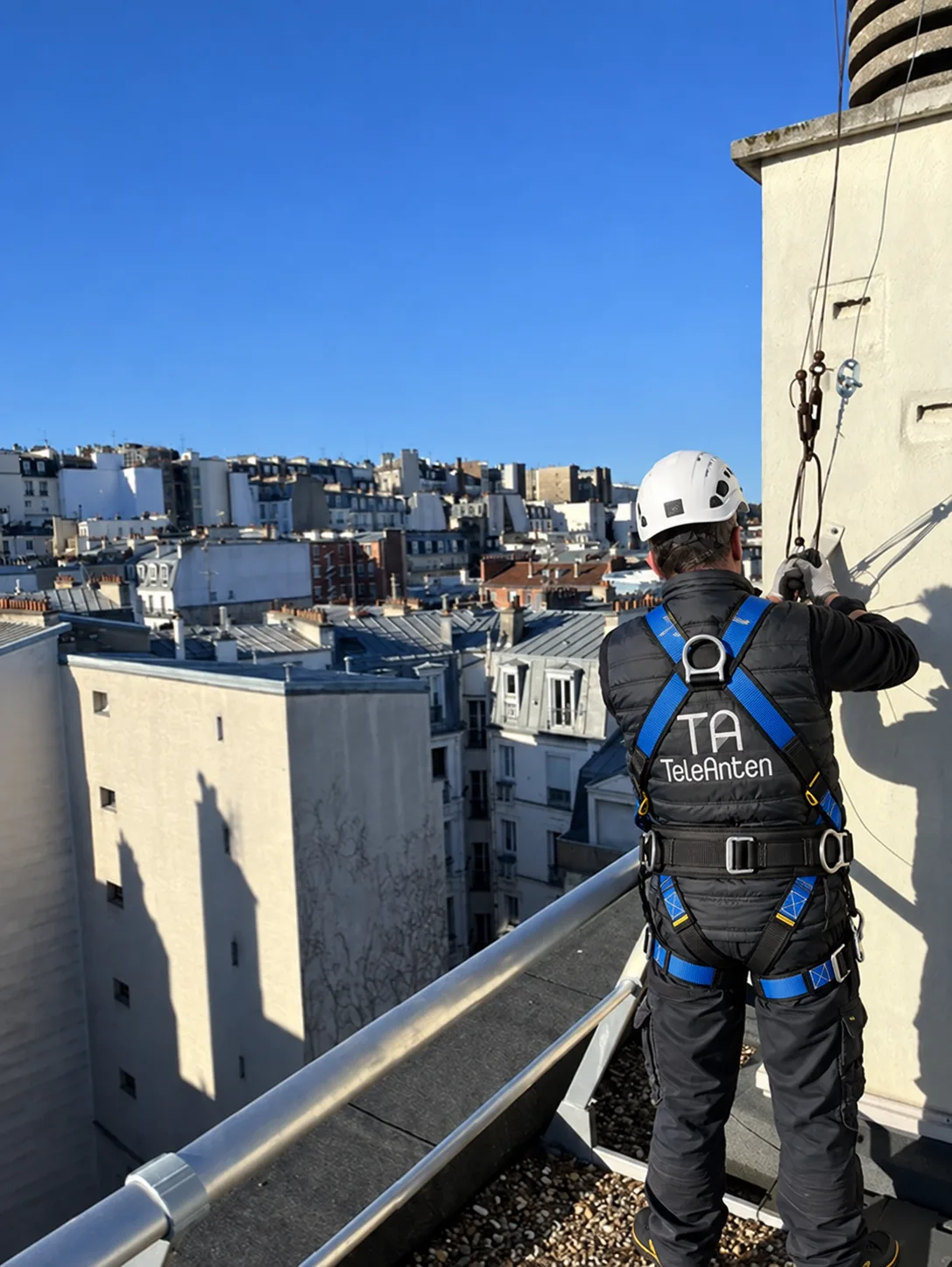 Antenniste TELEANTEN en gilet et harnais de sécurité intervenant sur la toiture d'un immeuble parisien